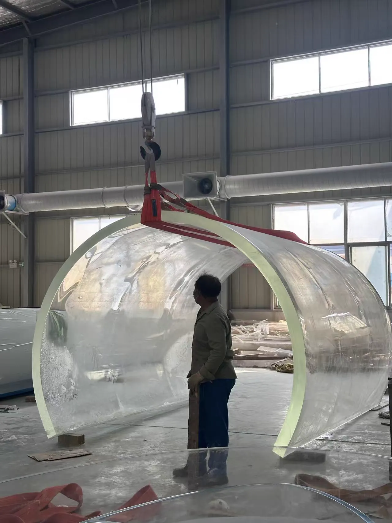 Worker guiding a large transparent curved acrylic shell during lifting
